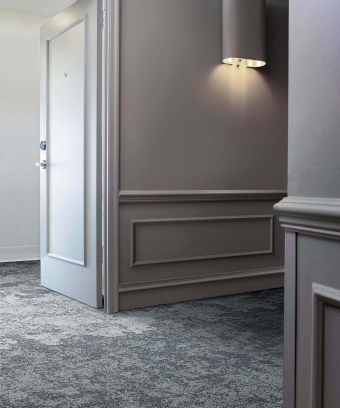 Victorex Interface Carpet Tiles Page Human Nature HN840 Nickel, in hotel hallway with hotel room door ajar Victorex Interface Carpet Tiles Page Human Nature HN840 Nickel, in hotel hallway with hotel room door ajar